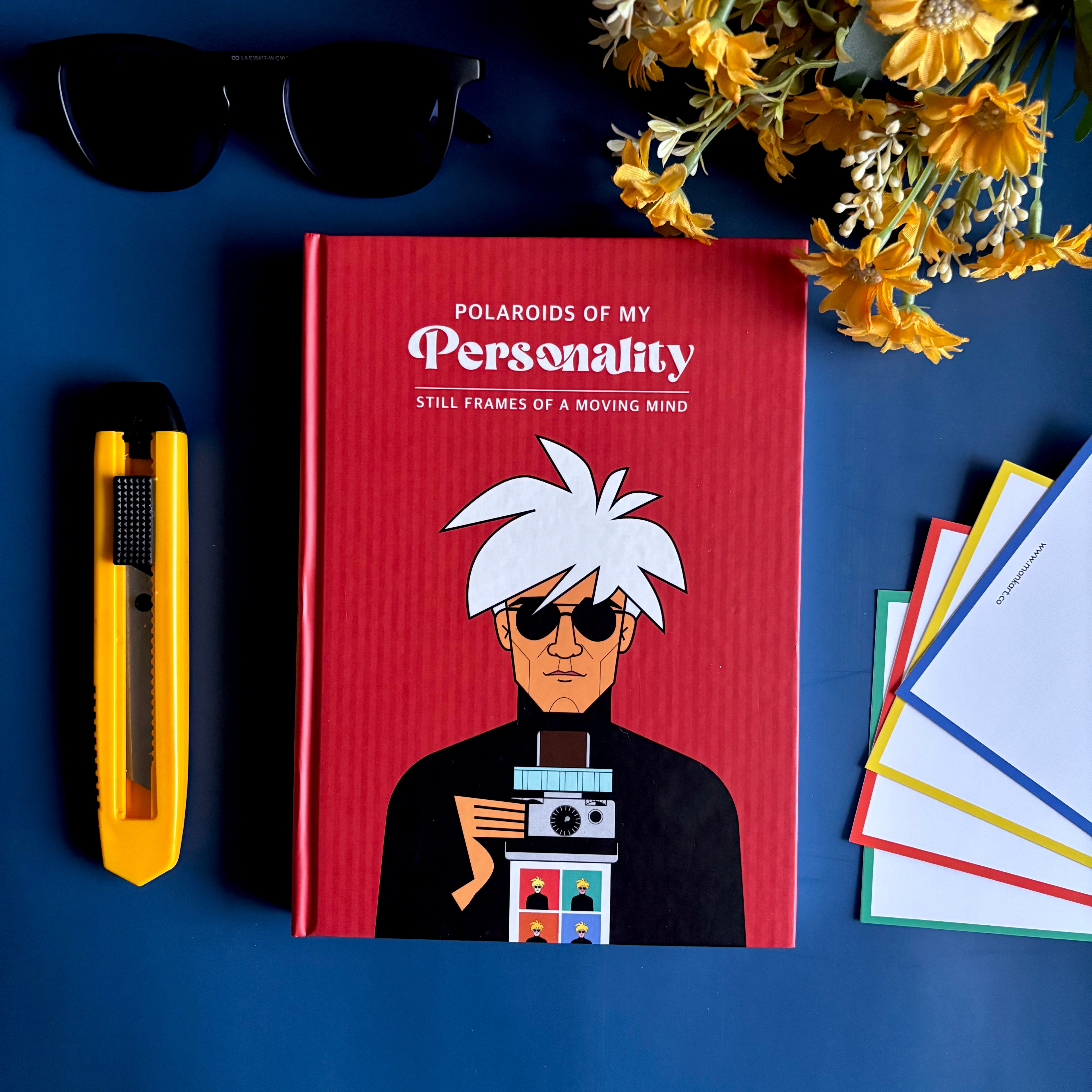 Red notebook titled 'Polaroids of My Personality' with an illustration of Andy Warhol on a blue background with sunglasses and flowers.  Designed by Monkart.