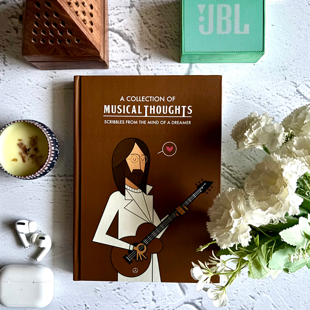Book titled 'A Collection of Musical Thoughts' with the Beatles start John Lennon holding a guitar on a white surface with a JBL speaker and flowers.  Designed by Monkart.