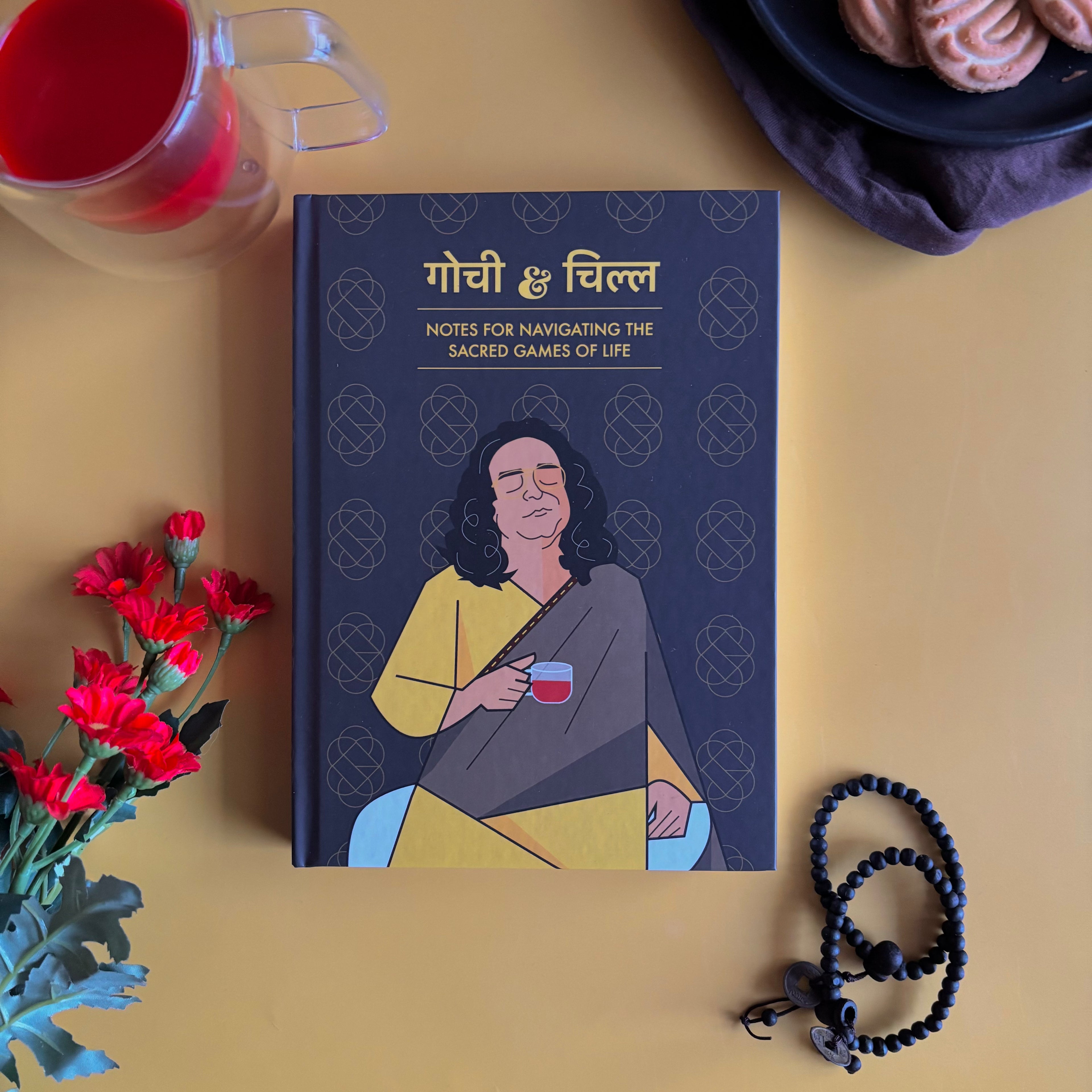 Notebook titled 'Gochi & Chill' inspired by Netflix TV Show Sacred Games with a person holding a cup on a yellow surface with flowers and a teacup.  Designed by Monkart.