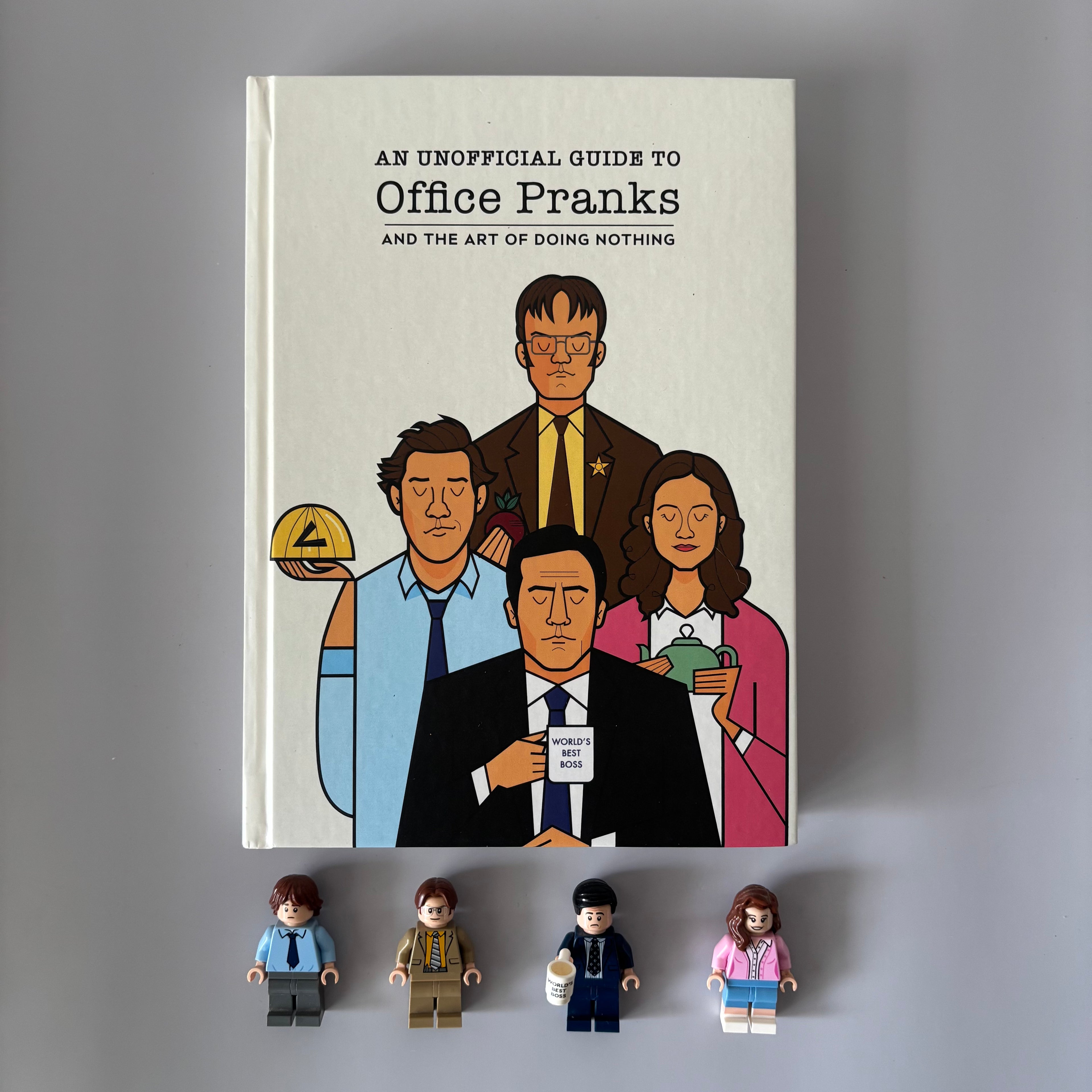 Book titled 'An Unofficial Guide to Office Pranks' with illustrations of office workers and mini figures on a gray background. Designed by Monkart.
